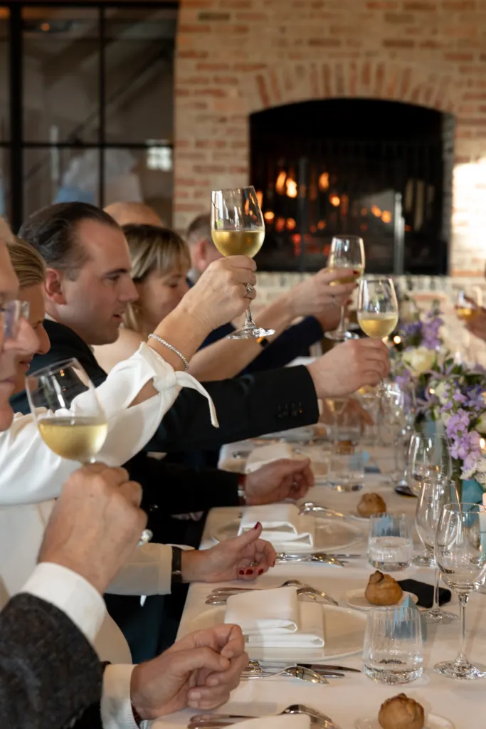 Gasten klinken aan een lange feesttafel bij de open haard