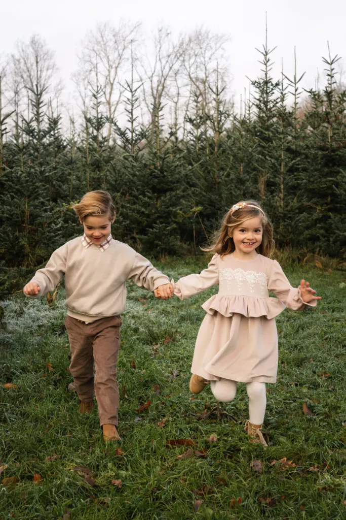 Twee kinderen lopen hand in hand tussen de kerstbomen