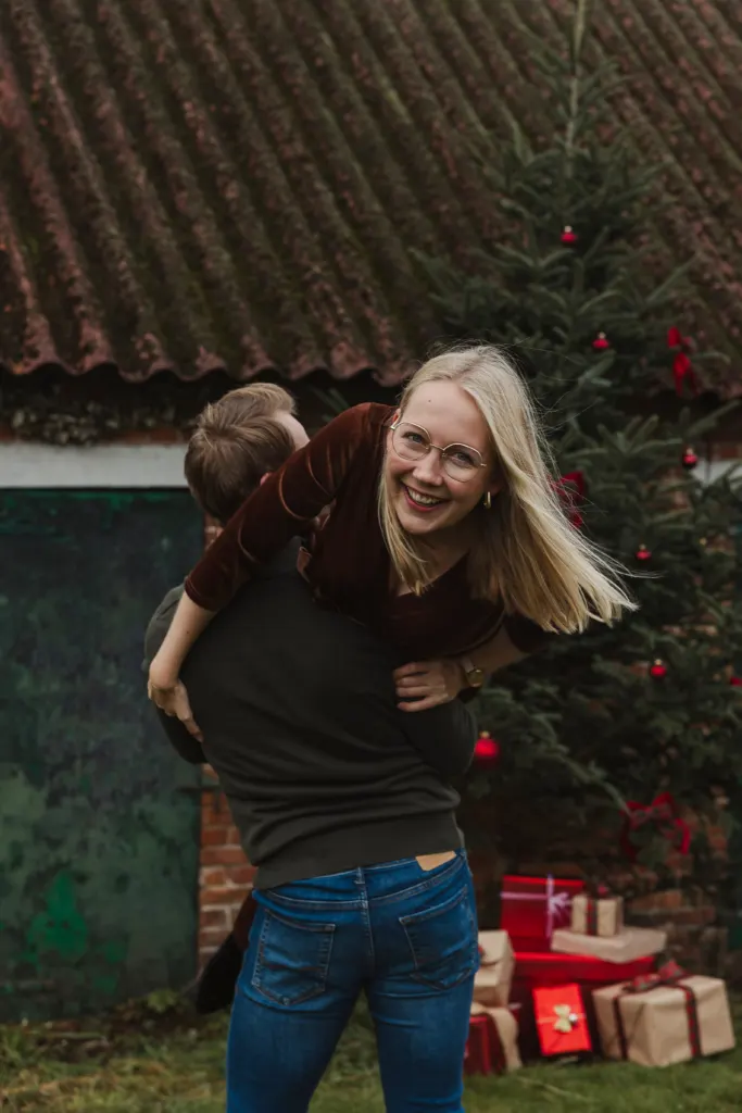 Moeder draagt haar kind op de rug bij de kerstboom