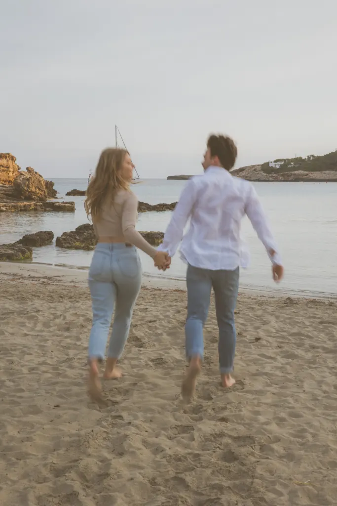 Koppel loopt hand in hand over een strand op Ibiza