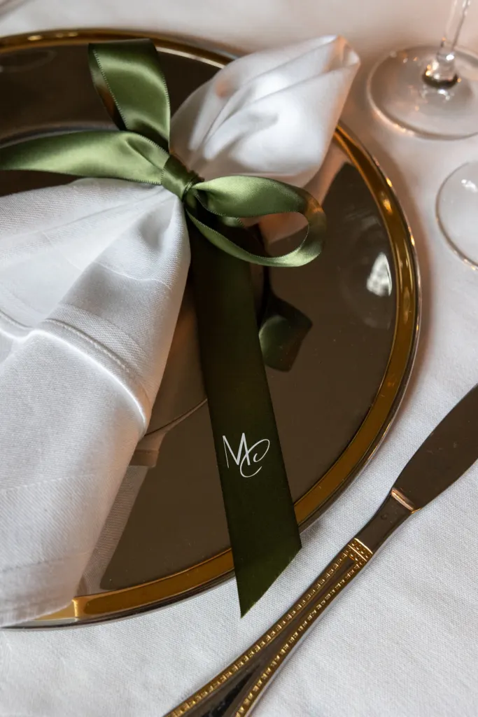 Gevouwen servet met groen lint en monogram op een gouden bord