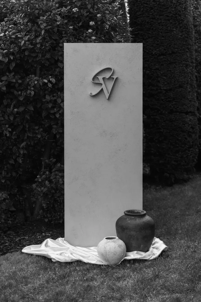 Stenen welkomstbord met monogram in een tuin, met vazen op wit satijn